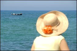 Woman with hat facing the sea with a boat